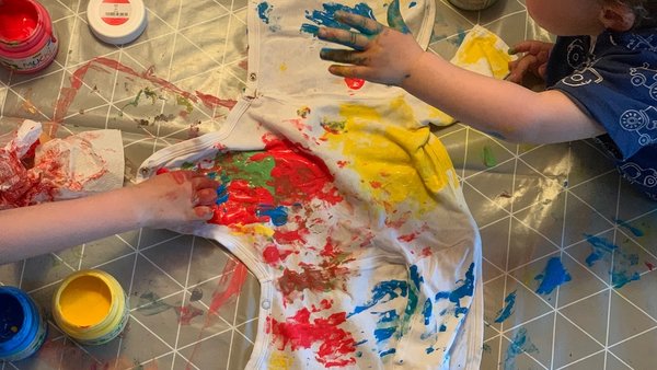 Zwei Kinder bemalen einen Babybody mit Fingerfarben